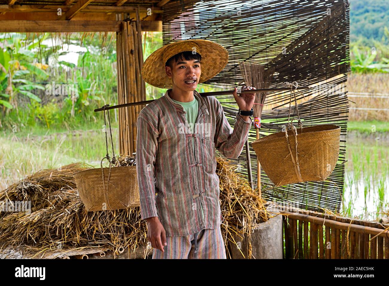Giovane uomo dimostrando il trasporto del riso con spallamento pole e due cestelli sospesi, riso tradizionale produrre tecnologia,Luang Prabang, Laos Foto Stock