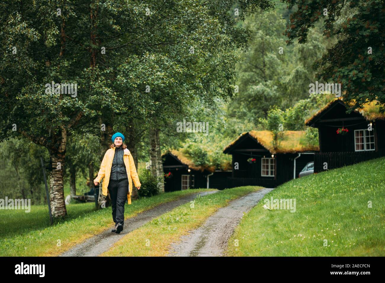 Giovane donna Lady turistiche a piedi vicino al tradizionale norvegese vecchie case in legno con il crescere dell'erba sul tetto. Cabine in Norvegia. Foto Stock