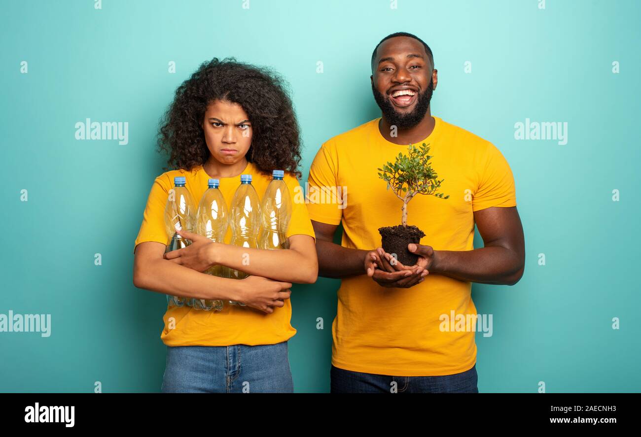 Inquinamento contro natura. Ragazza infelice con immondizia di plastica e ragazzo felice con un piccolo albero. Salvare il concetto del mondo Foto Stock
