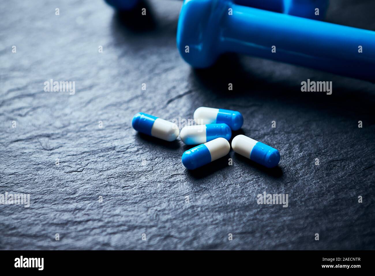 Sport supplementi (creatina capsule) e blu manubri in pietra scura sullo sfondo. Close up. Foto Stock