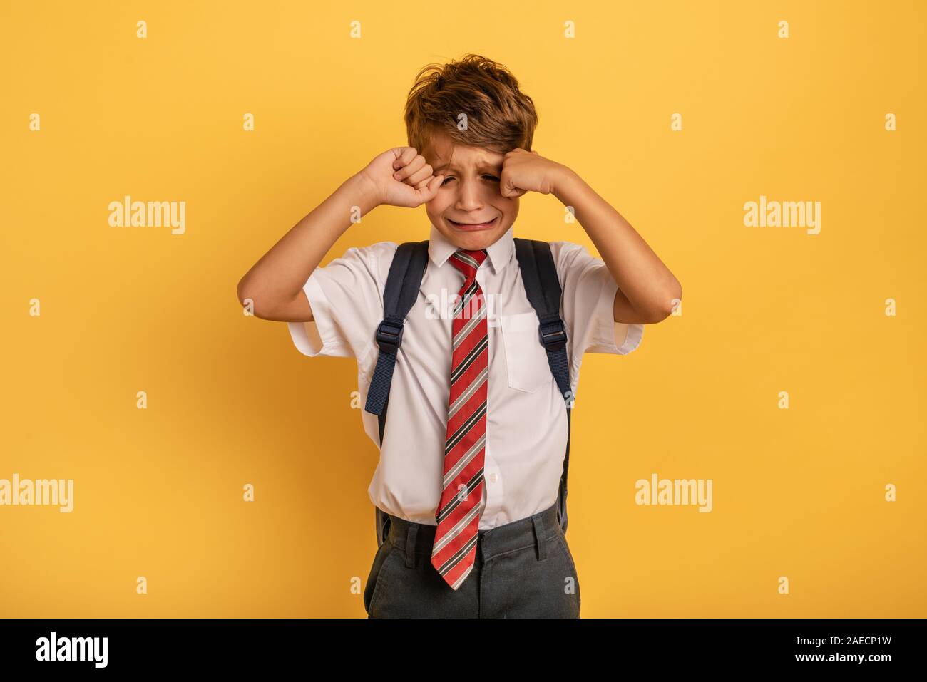 Bambino piange perché non vuole andare a scuola. Sfondo giallo Foto Stock