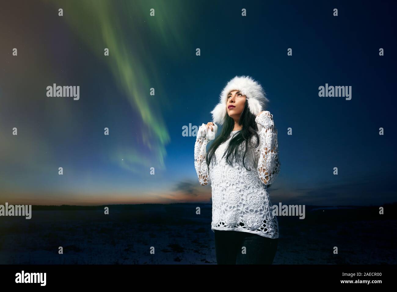 Bella ragazza in elegante Cappello invernale e bianco maglia camicetta sullo sfondo di Northern Lights nel cielo notturno. Bella Signora ammirando di inverno radiance e aurora. Concetto moderno di abbigliamento per camminare. Foto Stock