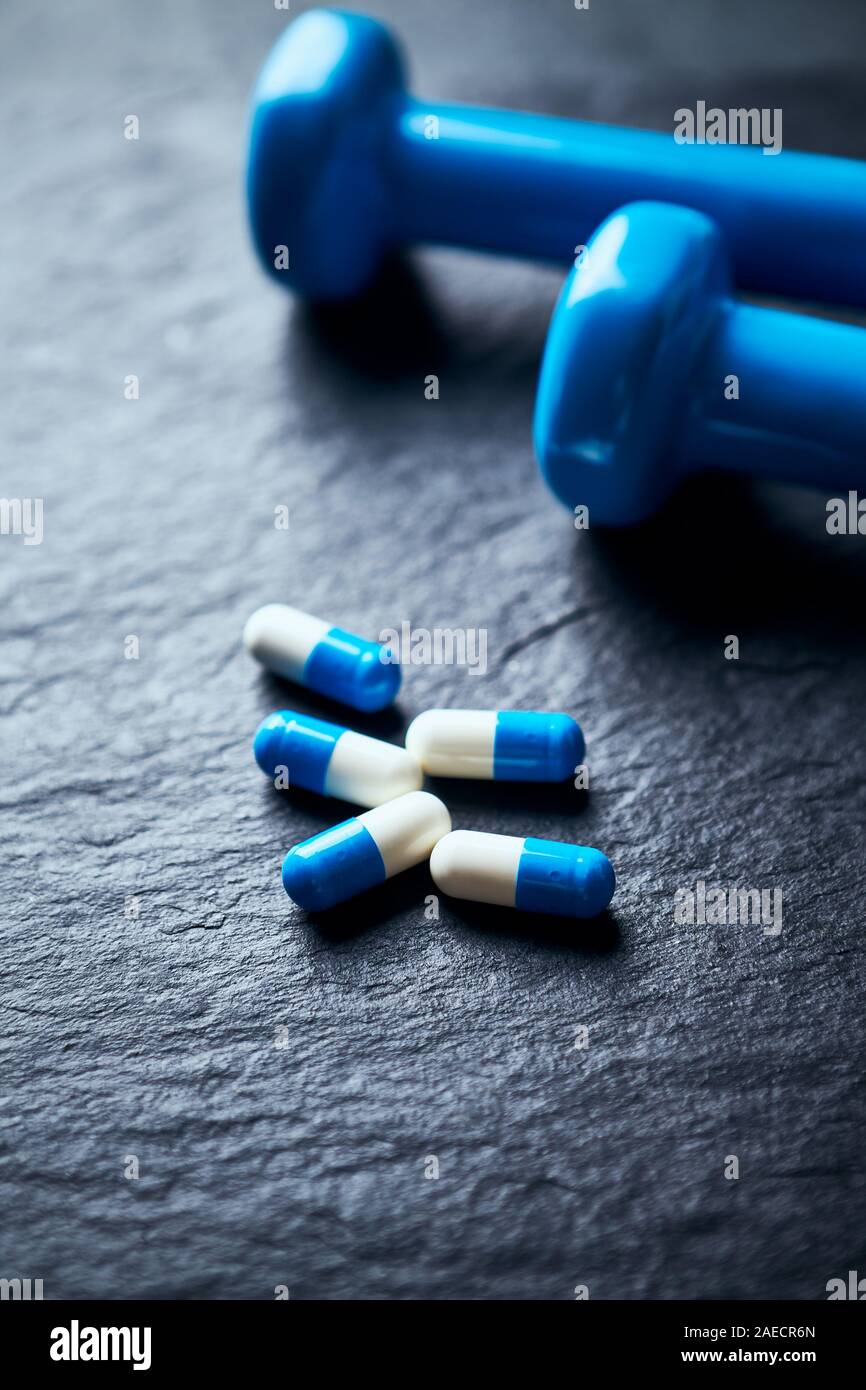 Sport supplementi (creatina capsule) e blu manubri in pietra scura sullo sfondo. Close up. Foto Stock