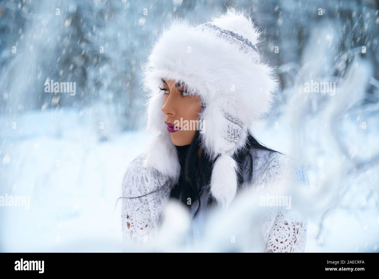 Bellissimo modello concepito in posa nella foresta invernale su sfondo sfocato. Attraente ragazza che indossa in warm white hat, bianco maglia blusa con perfetta compongono guardando lontano. Concetto di inverno cappelli. Foto Stock