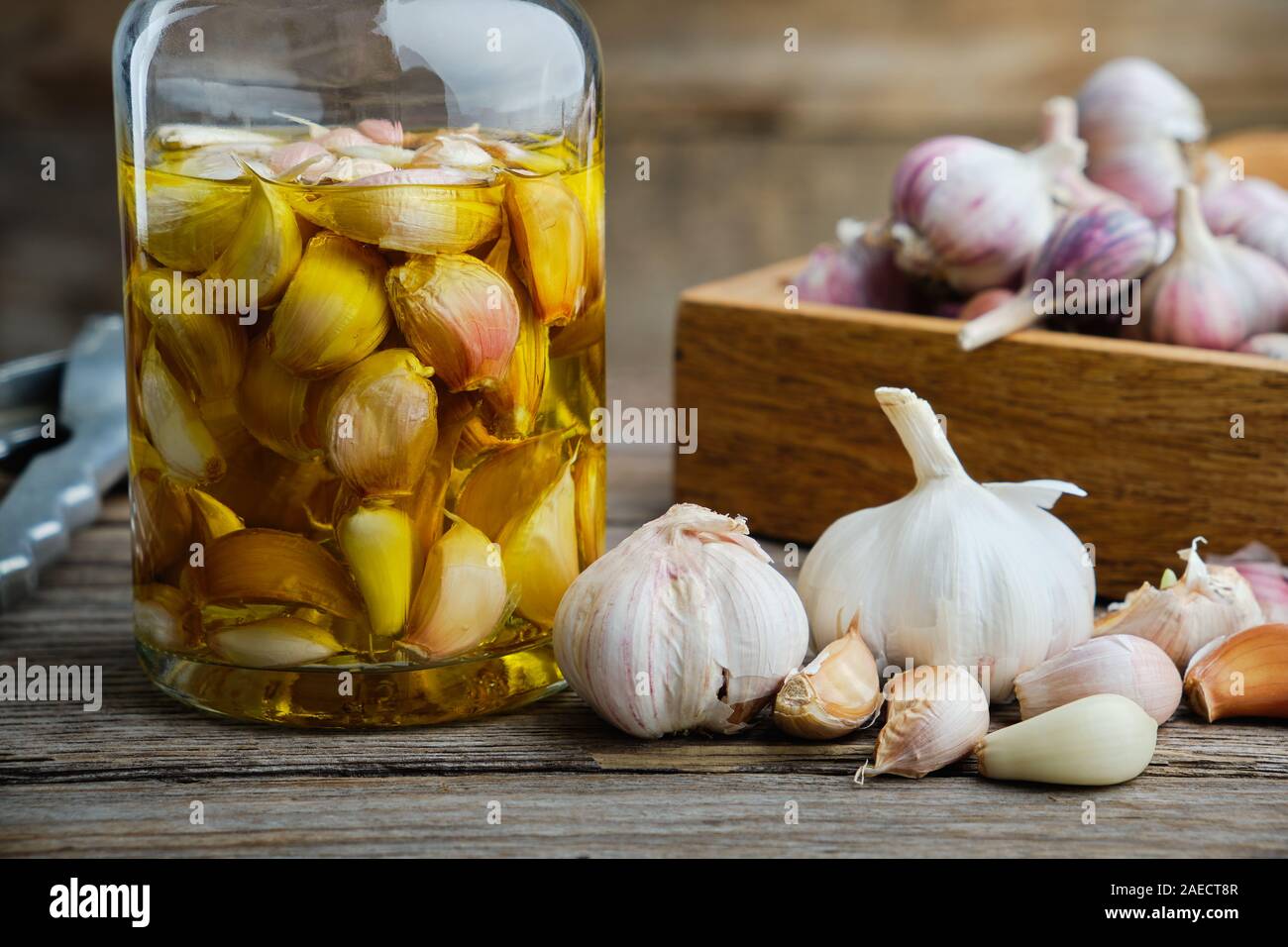 Aglio aromatico olio aromatizzato o bottiglia per infusione e casse di legno di spicchi di aglio in cucina in legno tavolo. Foto Stock