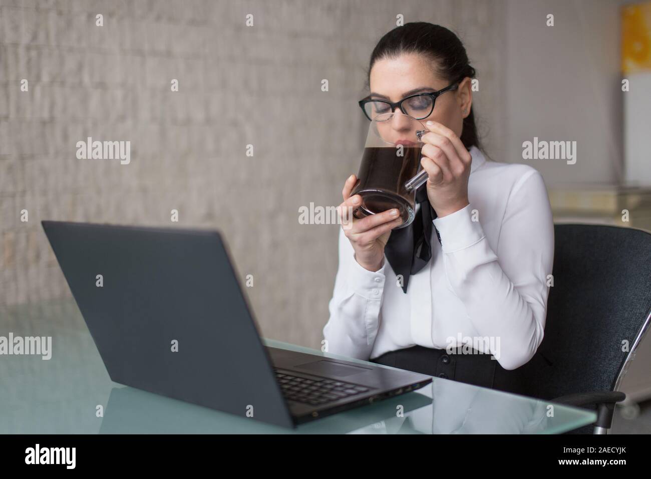 Giovane imprenditrice dipendente in abbigliamento formale di bere il caffè in ufficio a occhi chiusi Foto Stock