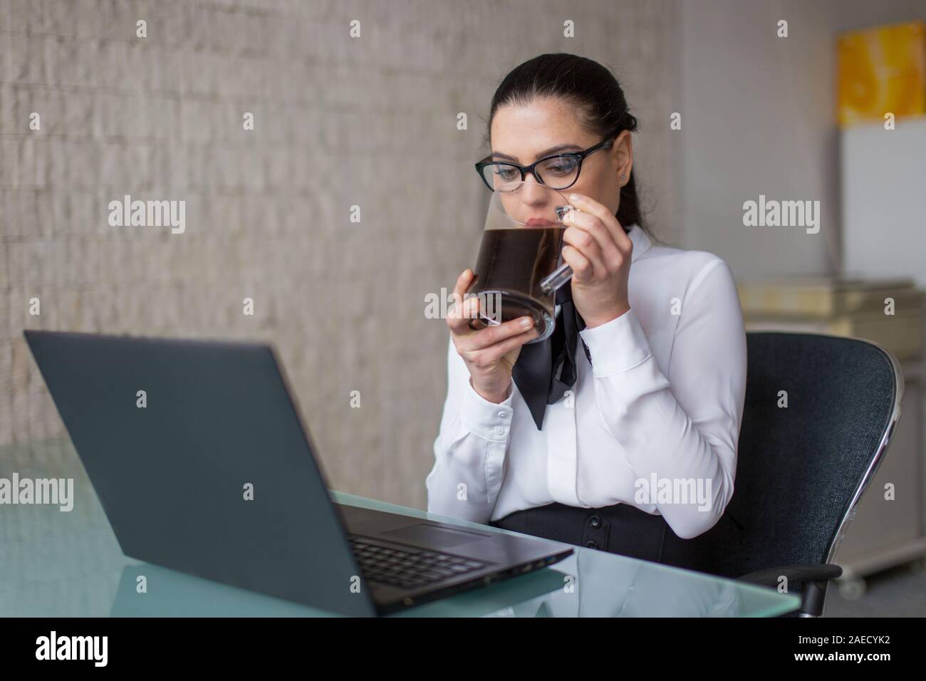 Giovane imprenditrice dipendente in abbigliamento formale di bere il caffè in ufficio Foto Stock
