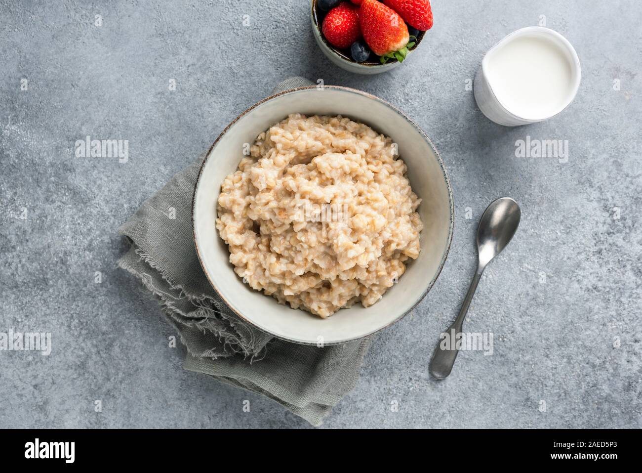 Sana colazione porridge di avena o farina di avena in un recipiente su calcestruzzo sfondo, table top view shot. Pulire il concetto di mangiare Foto Stock