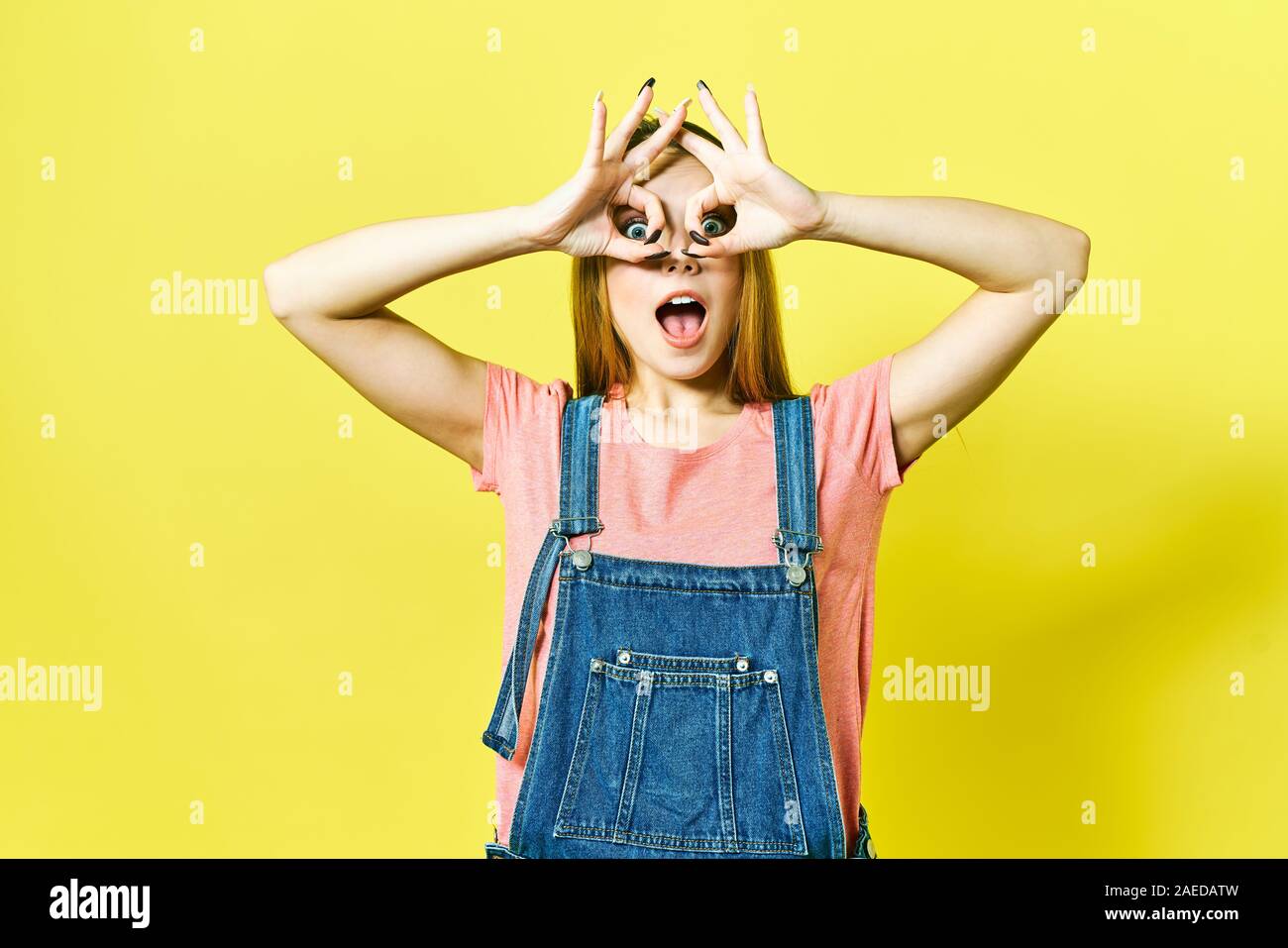 Divertente e gioiosa ragazza mostra okay segno winks e guardando la telecamera isolata su sfondo giallo. Foto Stock
