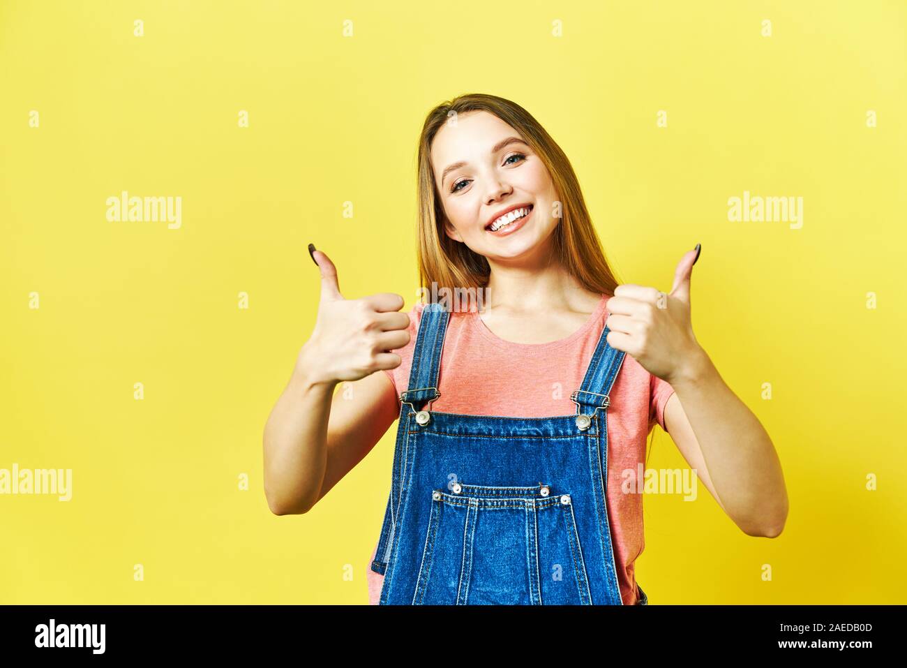 Felice Excited donna sorriso holding Thumbs up gesto, bella giovane donna sorriso guardando la fotocamera. isolato ob backgroud giallo. Foto Stock