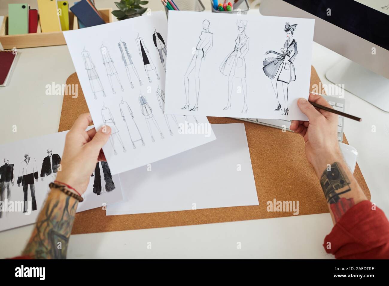 Close up tatuato maschio tenendo le mani schizzi di moda oltre il posto di lavoro in studio di design, spazio di copia Foto Stock