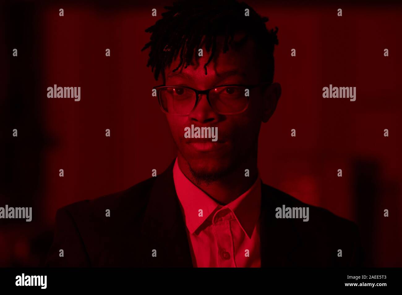 Testa e spalle ritratto di afro-americano alla moda uomo che indossa gli occhiali in posa lo sguardo lontano in illuminazione rossa, spazio di copia Foto Stock