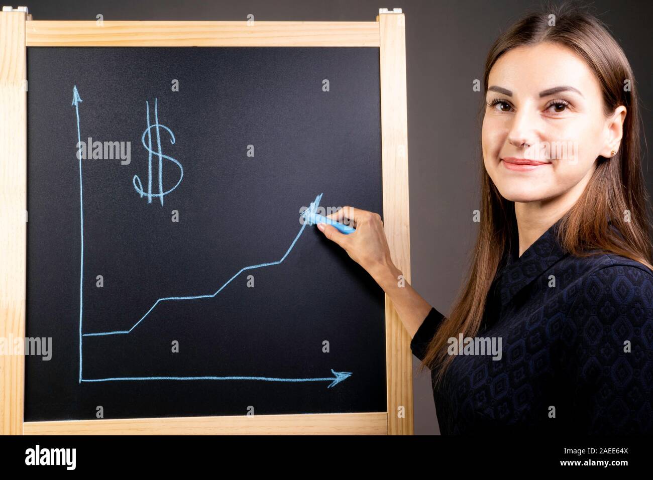Il grafico della crescita del dollaro è disegnato su una lavagna nera, una donna sorridente è in piedi vicino a. La valuta estera sul mercato finanziario Foto Stock