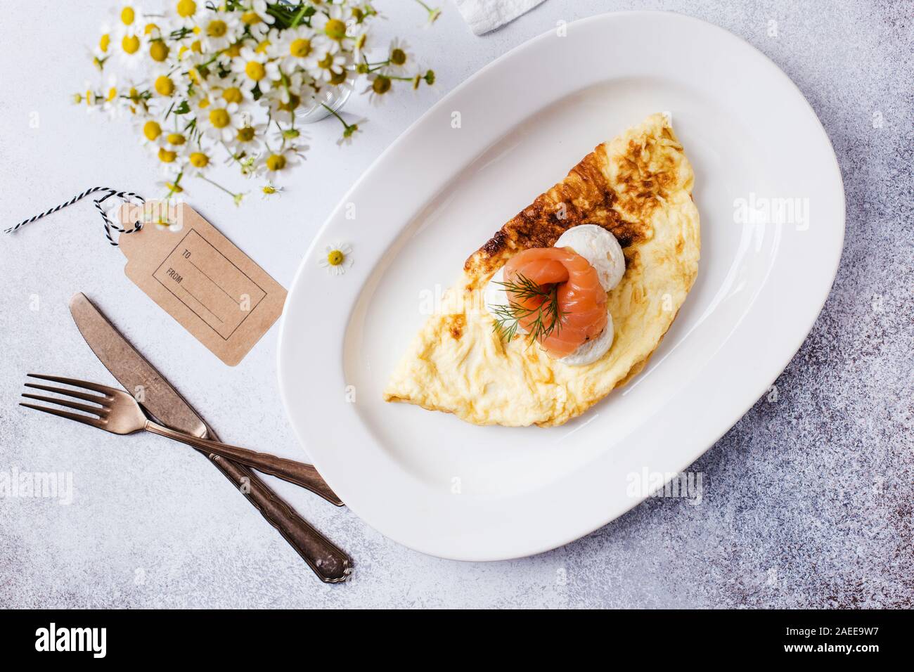 Il momento della colazione. Frittata con pesce rosso e margherite in un vaso su un grigio chiaro Tavolo con uno sfondo a trama. Foto Stock