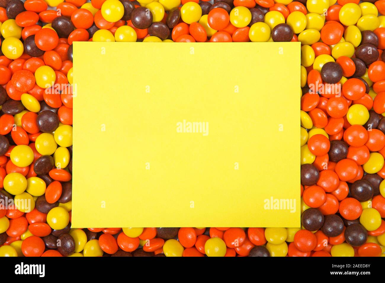 Sfondo di candy cioccolatini rivestito in arancione, giallo e marrone scuro, halloween colori per le vacanze. scheda gialla nella parte centrale con spazio di copia Foto Stock