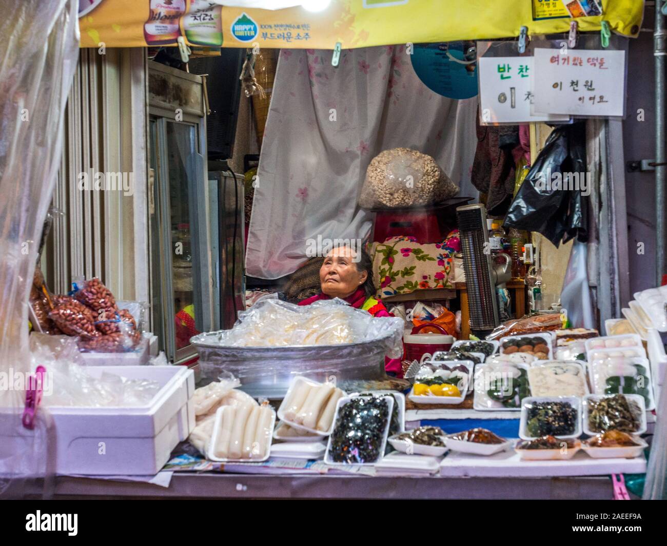 Donna venditore, seduti dietro il cibo in stallo, Tongin Mercato, Seoul, Corea del Sud. Foto Stock
