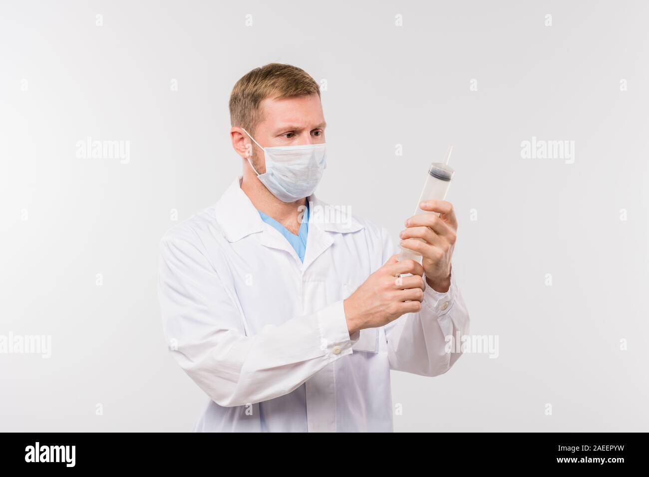 Giovane maschio medico in camice bianco e la maschera protettiva tenendo la siringa grande Foto Stock