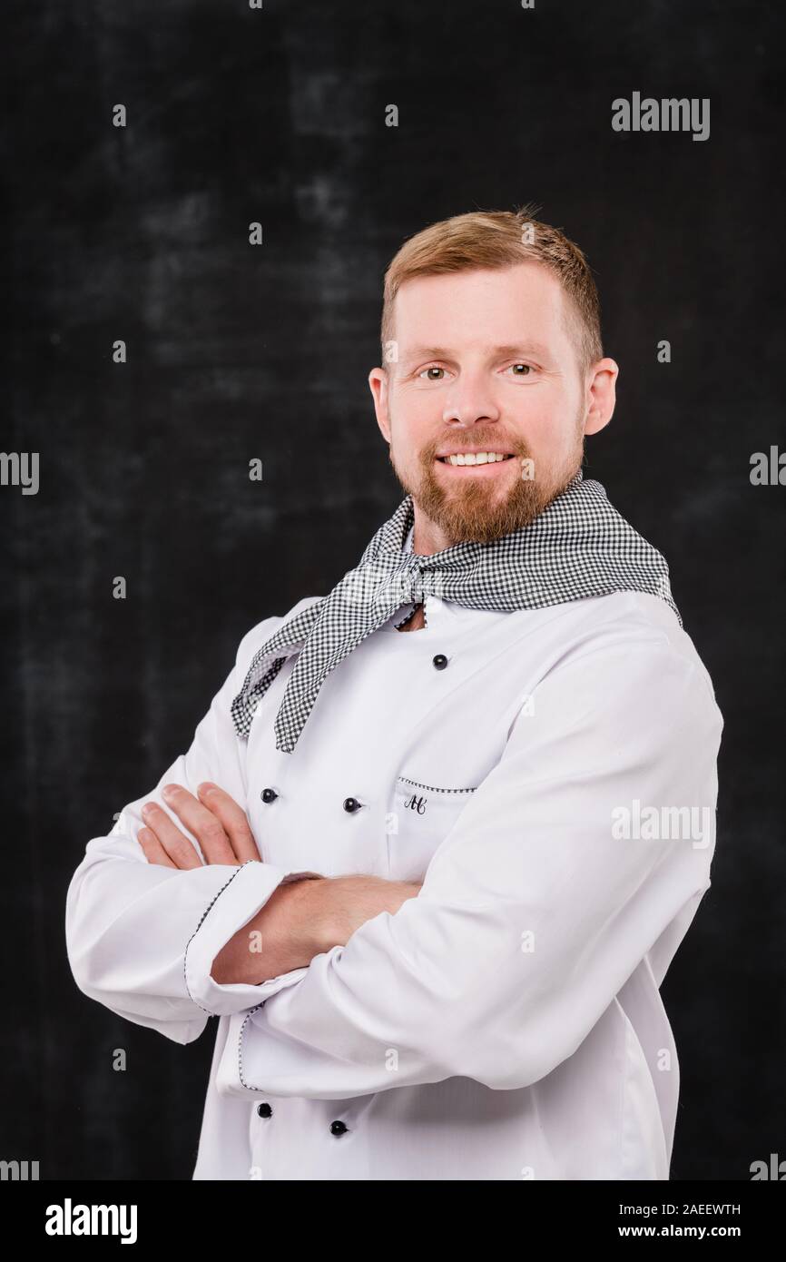 Felice giovane maschio barbuto chef in uniforme che vi guardano con sorriso toothy Foto Stock