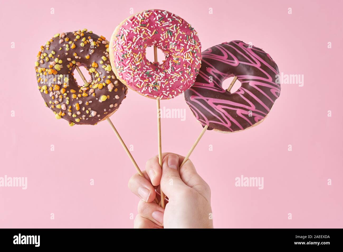 Tre le ciambelle nella donna la mano su sfondo rosa. Cucina creativa stile minimalista Foto Stock