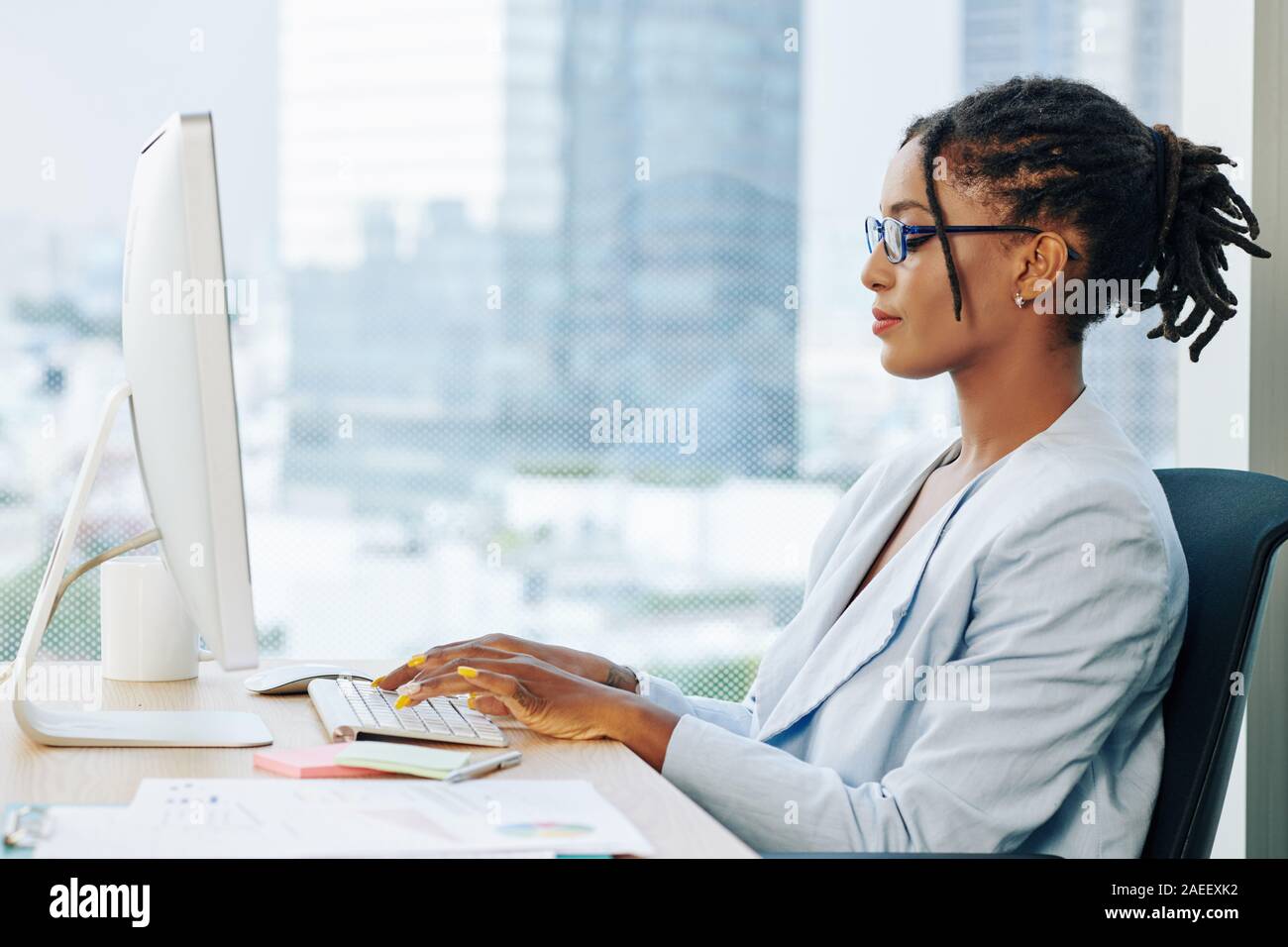 Elegante giovane imprenditrice ispanica con dreadlocks con gli occhiali quando si lavora sul computer portatile in ufficio Foto Stock