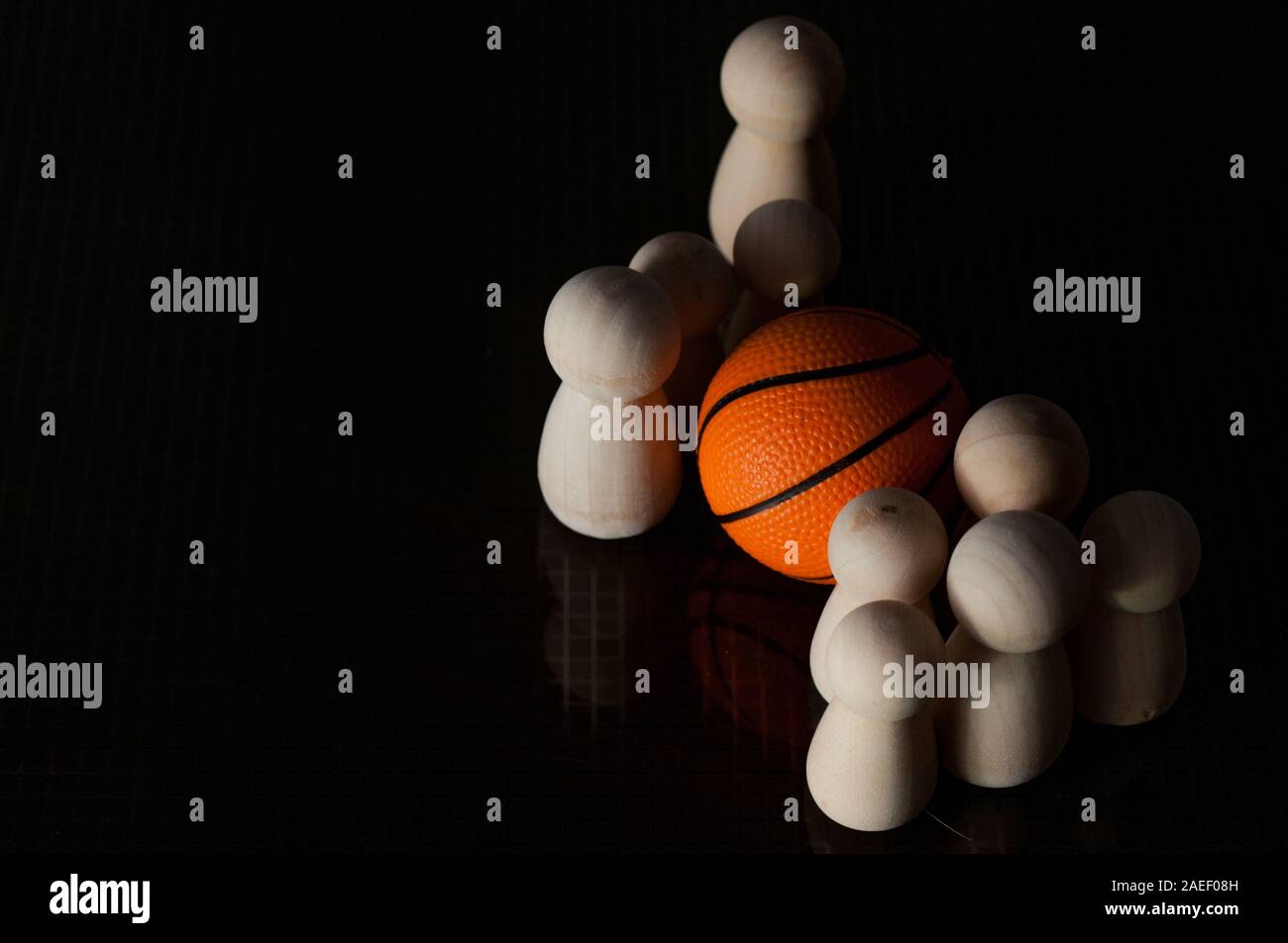 Pedine in legno e una palla da basket su uno sfondo nero. basket concept. Riprodurre il concetto. Foto Stock
