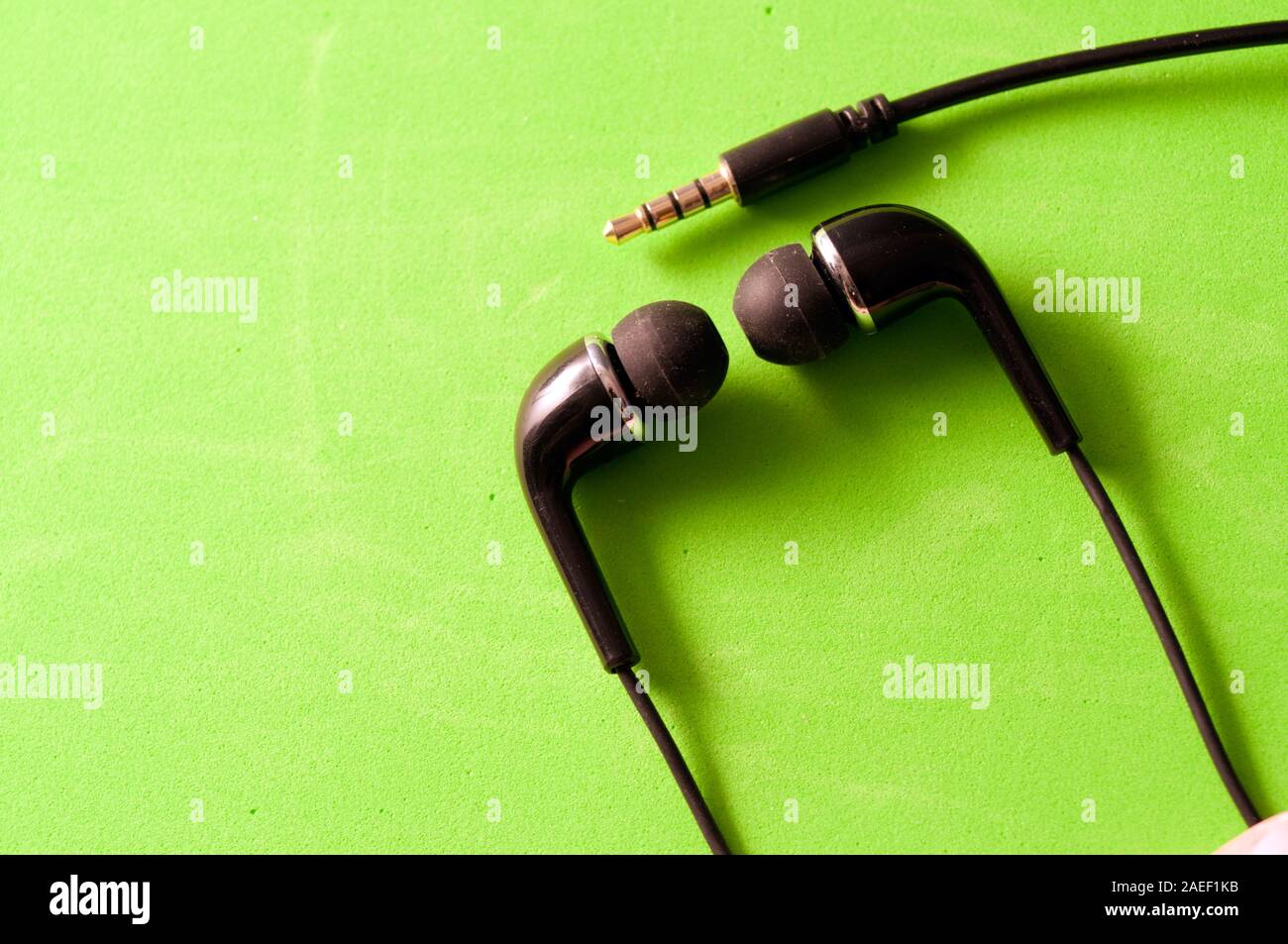 Gli auricolari di colore nero e jack per il collegamento isolato su sfondo verde Foto Stock