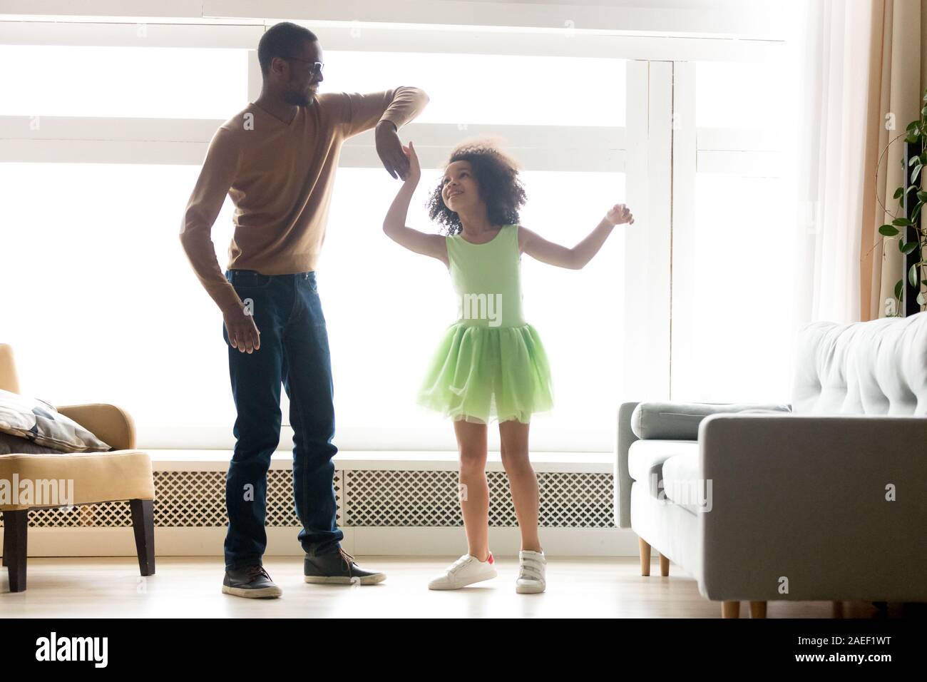 Felice papà nero ballando con la figlia nel verde mantello di balletto Foto Stock