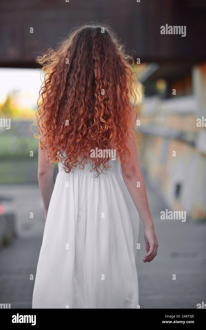Vista posteriore della bella donna che indossa lungo abito bianco, con lunghi capelli ricci Foto Stock