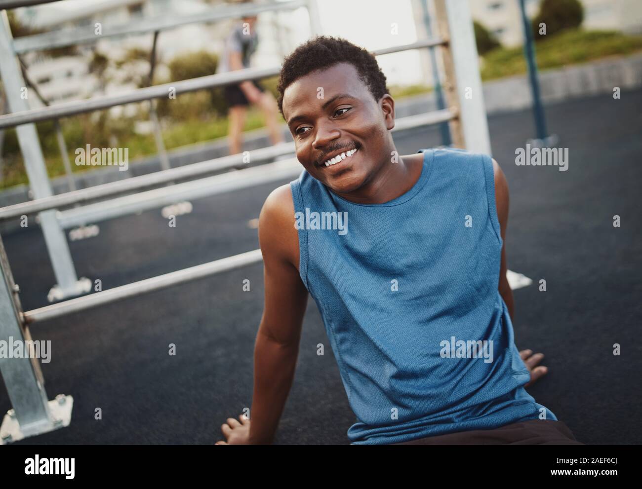 Allegro giovane fitness sportivo a riposo dopo la formazione presso la palestra esterna park seduto a terra sorridente e guardando lontano Foto Stock