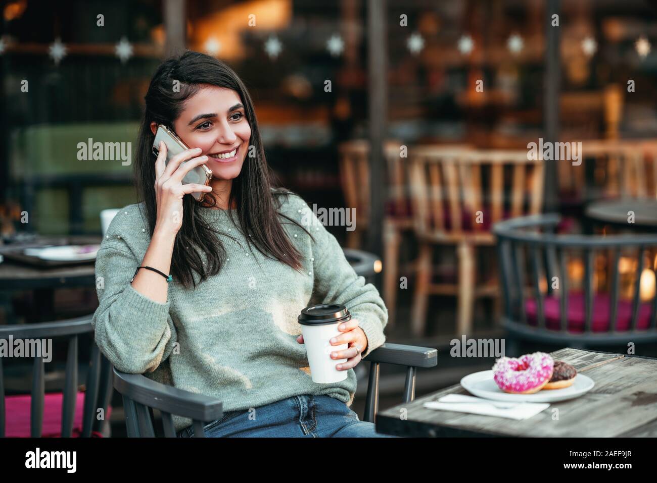Giovane donna è seduto in un bar e parlando con il telefono cellulare con un sorriso. Foto Stock