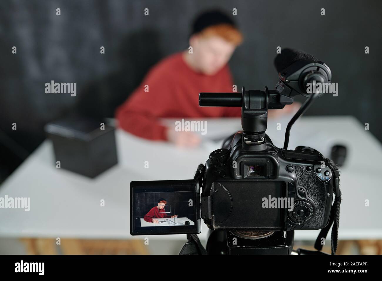 Schermata della videocamera nella parte anteriore del giovane maschio vlogger seduto da scrivania Foto Stock