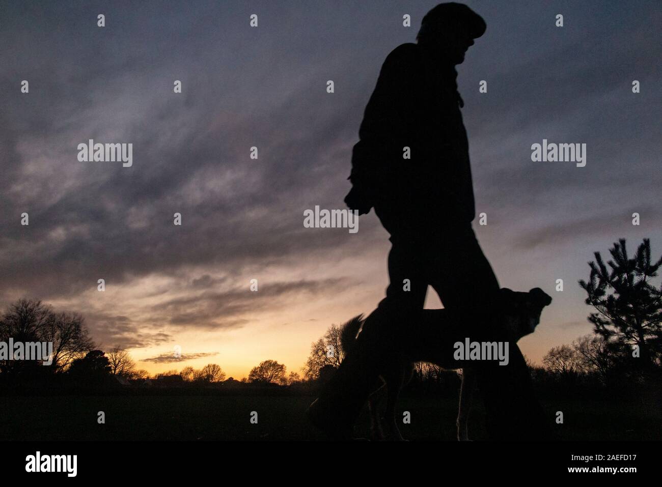 Un uomo cammina il suo cane con un tramonto in un parco di Londra Foto Stock