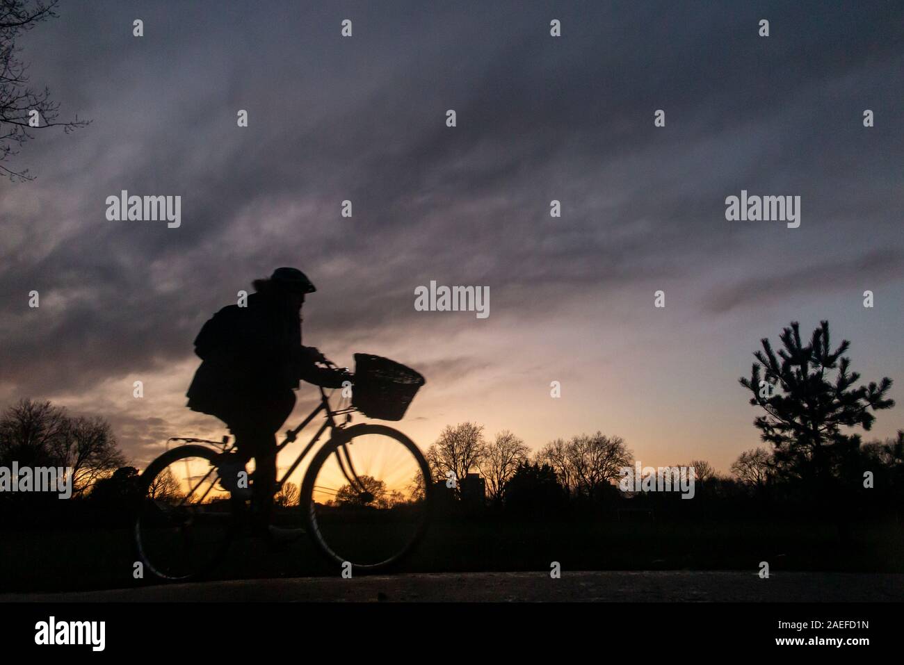 Un ciclista cavalca la sua moto con una impostazione di sole in un parco di Londra Foto Stock