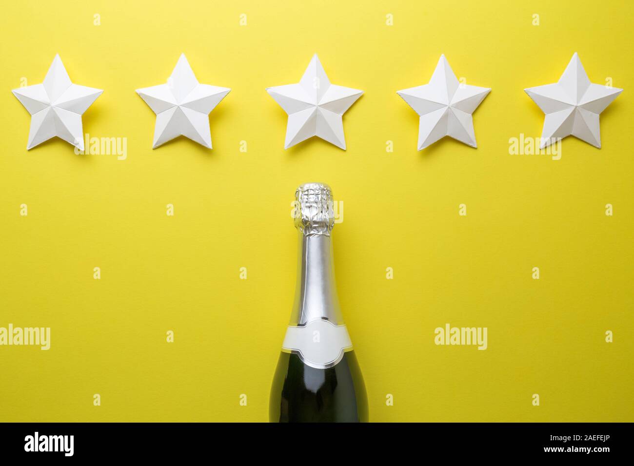 Piatto di laici bottiglia di champagne e cinque stelle di carta su sfondo giallo minimo concetto creativo. Foto Stock