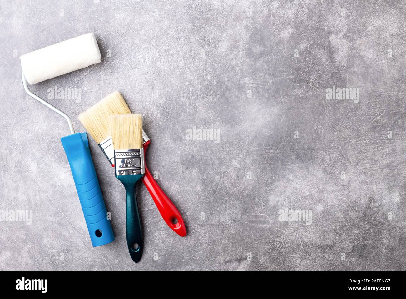 Rullo di vernice e due spazzole su sfondo grigio. Vista da sopra con copia spazio. Foto Stock