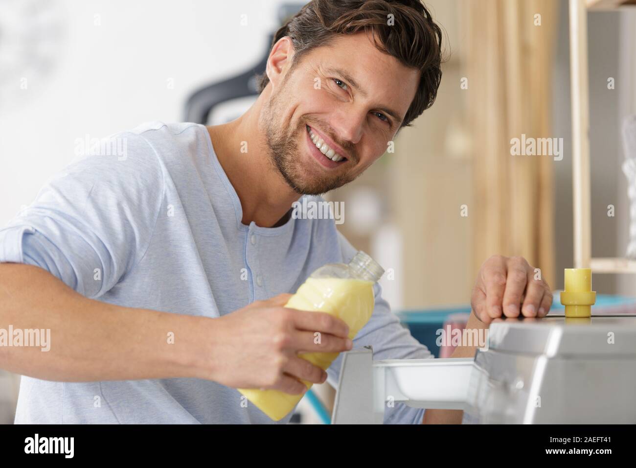 Uomo felice di aggiungere liquido alla macchina di lavaggio Foto Stock