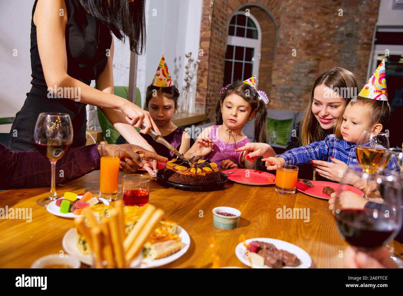 Ritratto di felice famiglia multietnica celebra un compleanno a casa. La famiglia grande torta di mangiare e di bere il vino durante il messaggio di saluto e il divertimento dei bambini. Celebrazione, famiglia, gruppo, home concetto. Foto Stock