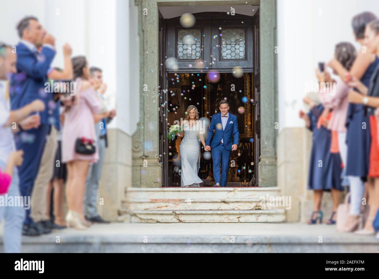 Sposi novelli uscendo dalla chiesa dopo la cerimonia di matrimonio, la famiglia e gli amici per celebrare il loro amore con la doccia di bolle di sapone, minando personalizzato Foto Stock