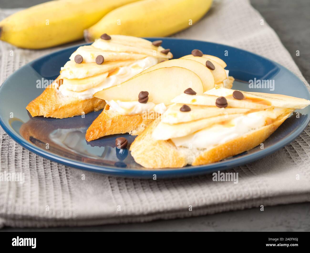 Piastra di colore blu con un tre toast alla francese con banane, pere, crema di formaggio, gocce di cioccolato, sciroppo di caramello, vista laterale Foto Stock