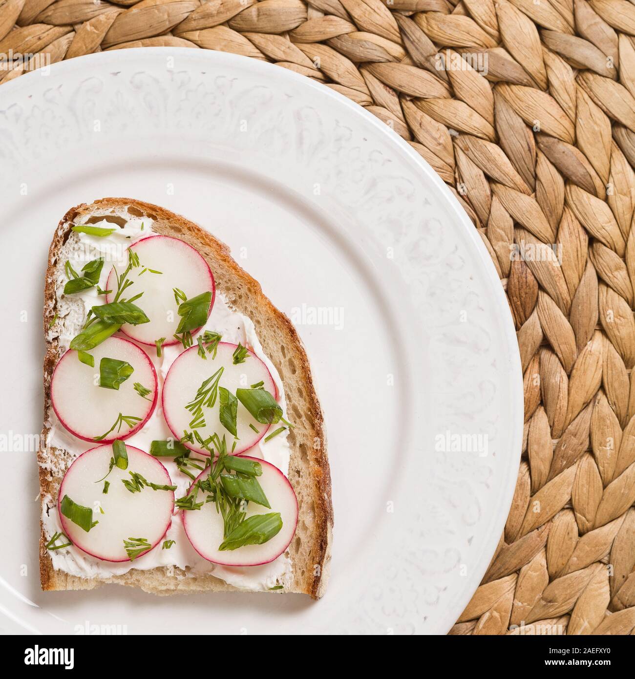 Vista dall'alto sul sandwich integrali con rafano organico e la crema di formaggio sulla piastra bianca e paglia tabella MAT. Cibo sano per la prima colazione o uno spuntino. Vegetari Foto Stock