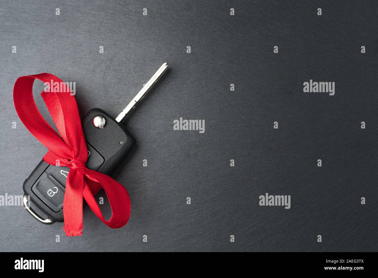 Chiave auto con fiocco rosso su nero scuro piastra di ardesia sfondo. Il Natale o il giorno di San Valentino regalo o presente concetto astratto. Copia spazio sulla destra. Fla Foto Stock