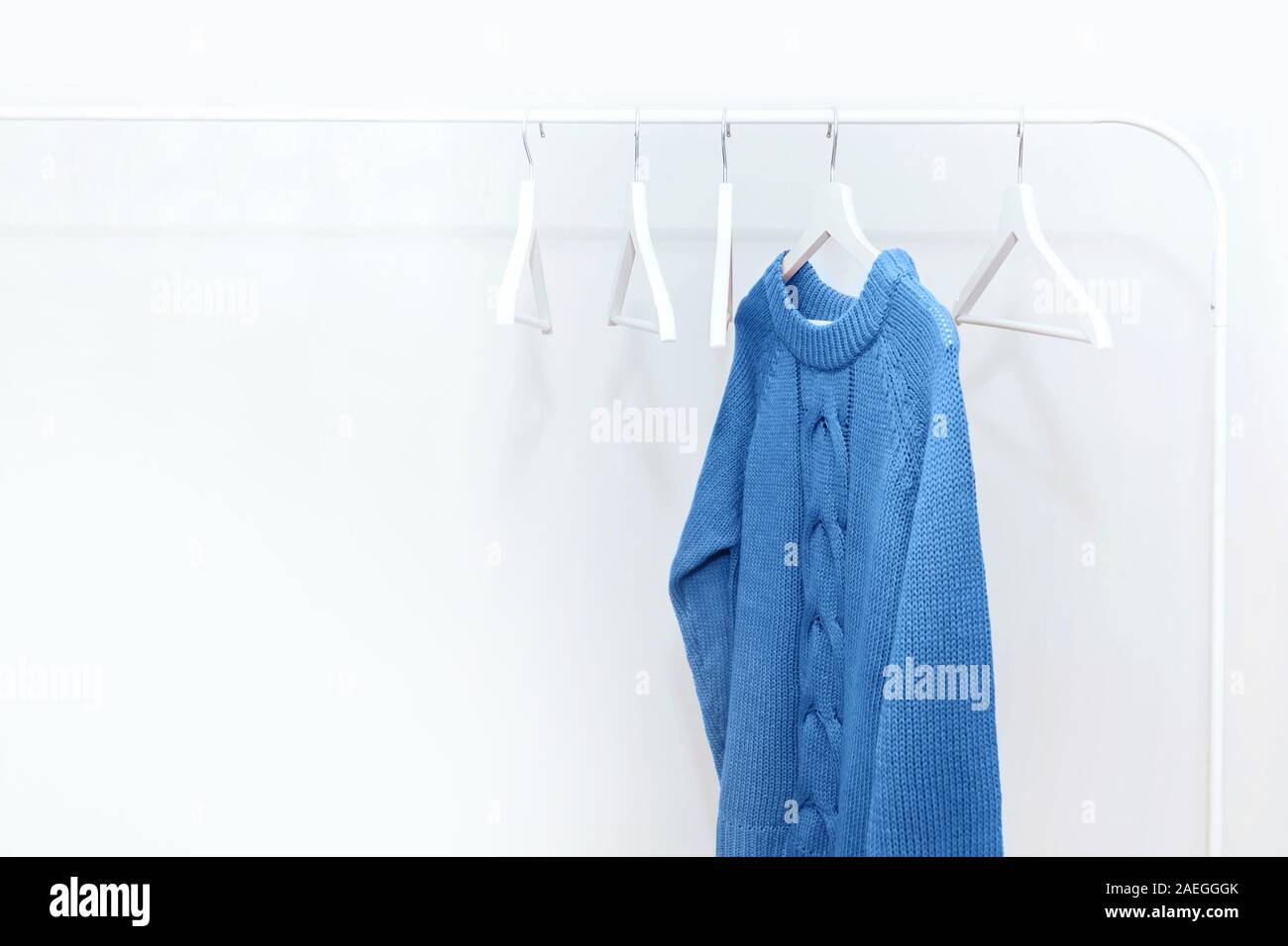 Uno blu classico a maglia maglione caldo su bianco appendiabiti e molti grucce vuote. Foto Stock