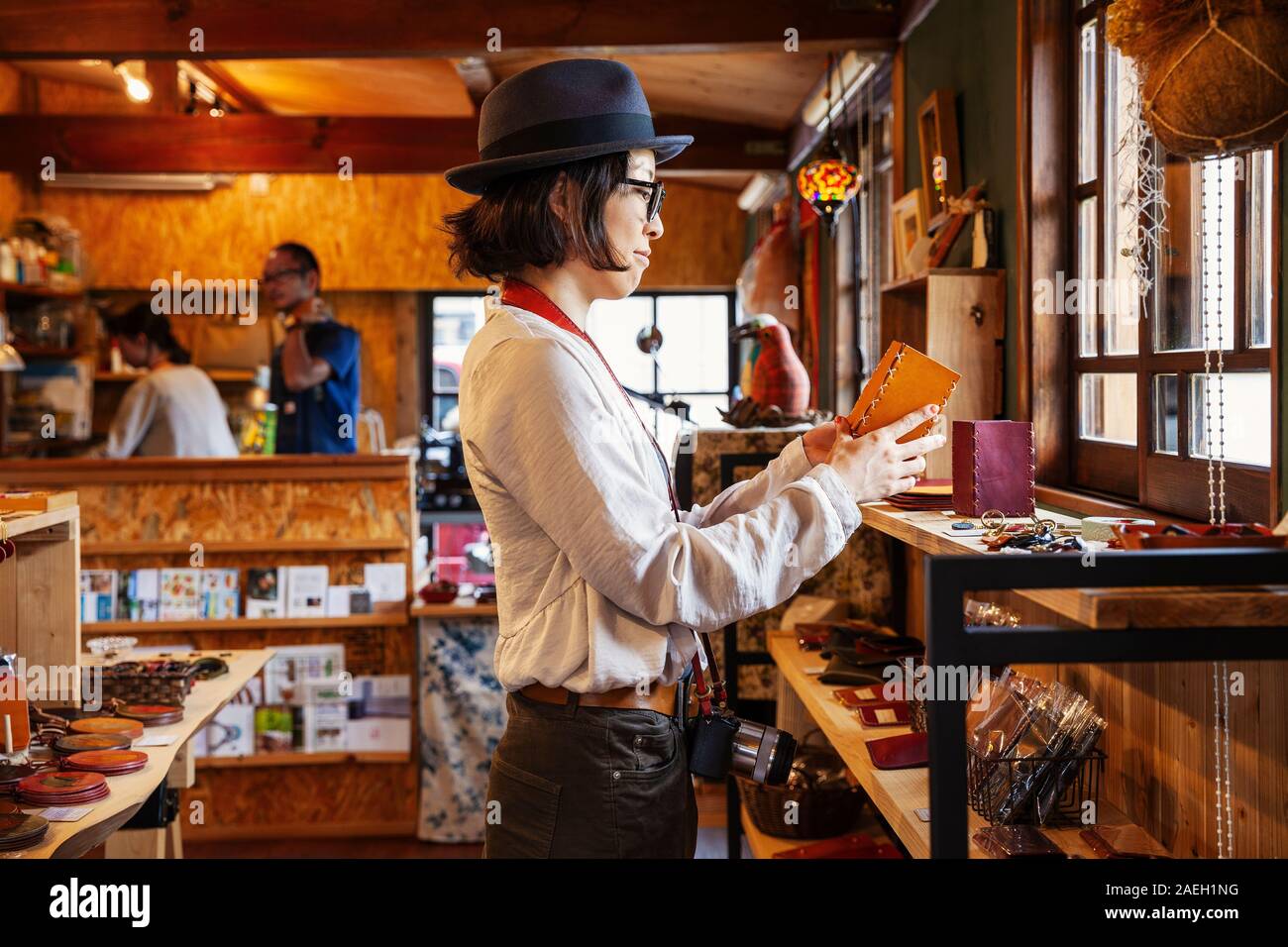 Donna Giapponese che indossa un cappello e occhiali navigando la merce in un negozio di cuoio. Foto Stock