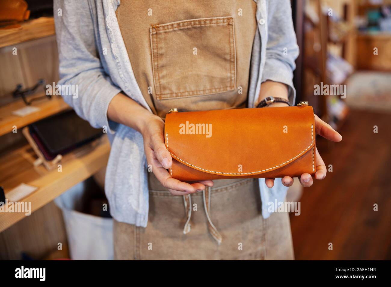 Close up della donna in piedi in un negozio di cuoio, tenendo in pelle marrone pochette. Foto Stock
