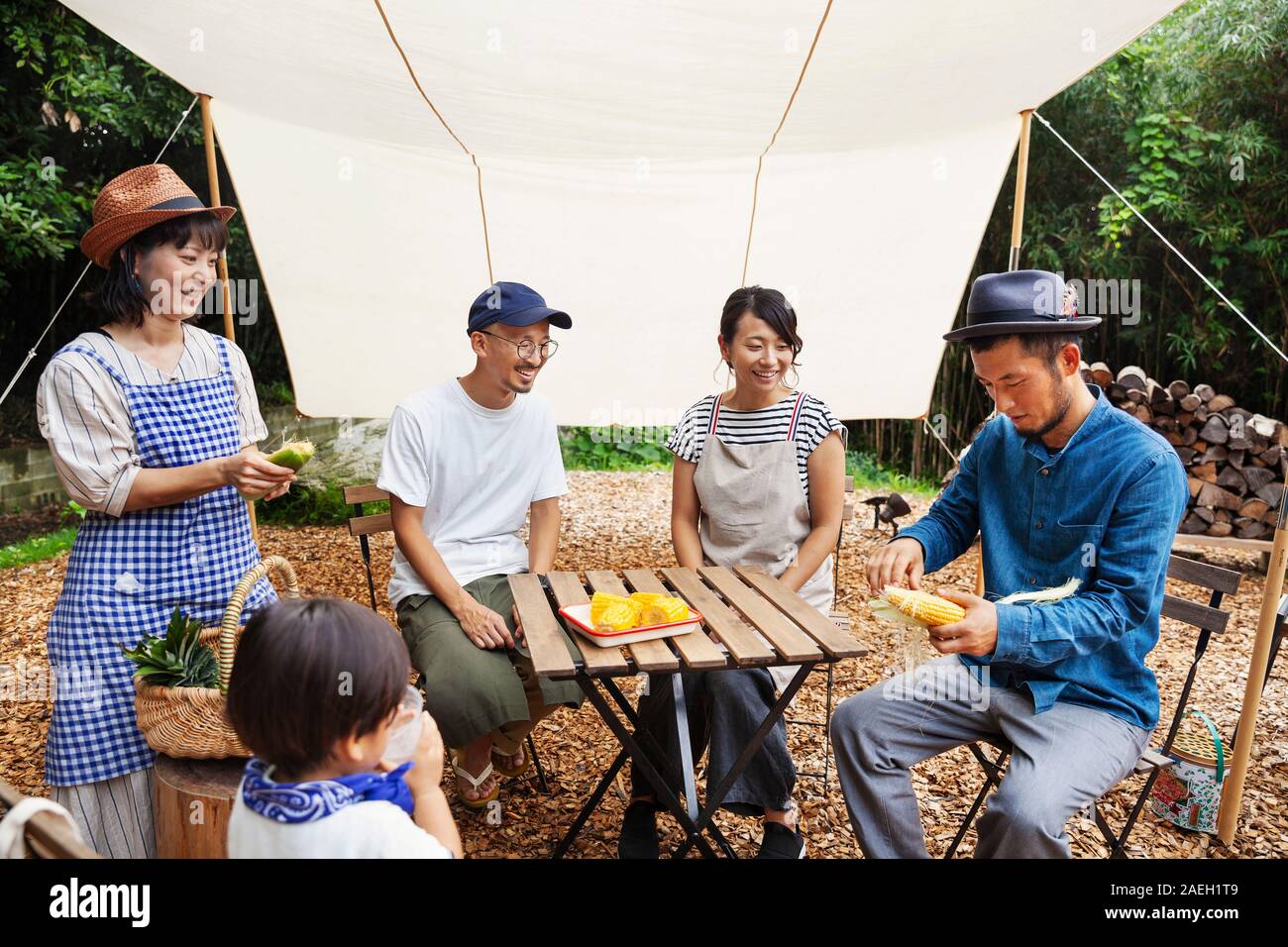 Gruppo di giapponese uomini e donne e il ragazzo si sono riuniti intorno ad un tavolo sotto una tettoia, preparare verdura. Foto Stock
