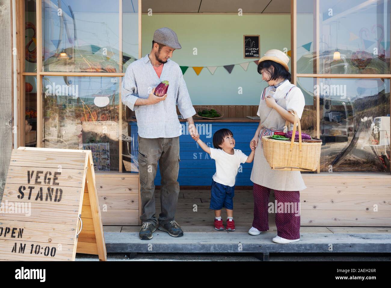Giapponese uomo, donna e bambino in piedi al di fuori di una farm shop, tenendo le mani. Foto Stock