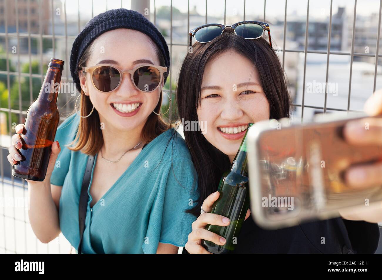 Due giovani donne giapponesi seduto su un tetto in un contesto urbano, tenendo selfie con il telefono cellulare. Foto Stock