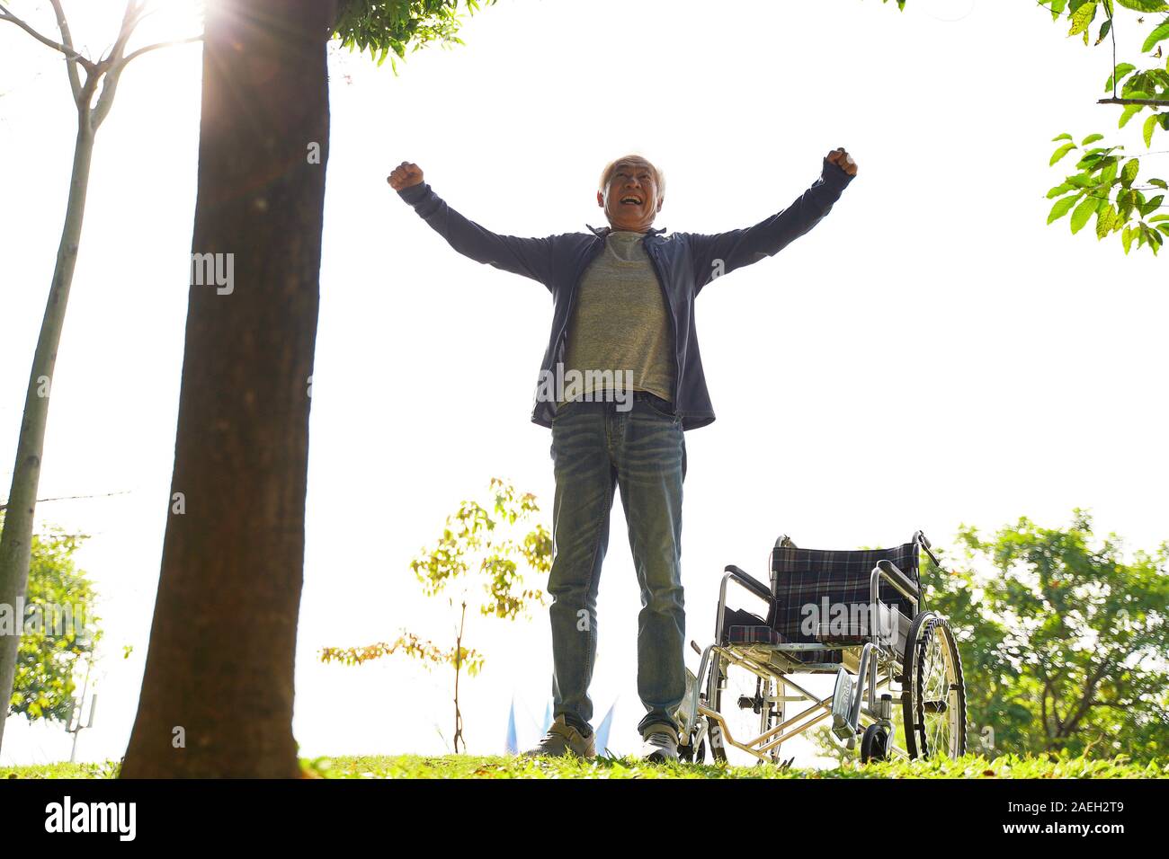 Asian senior uomo in piedi dalla sedia a rotelle con le braccia aperte Foto Stock