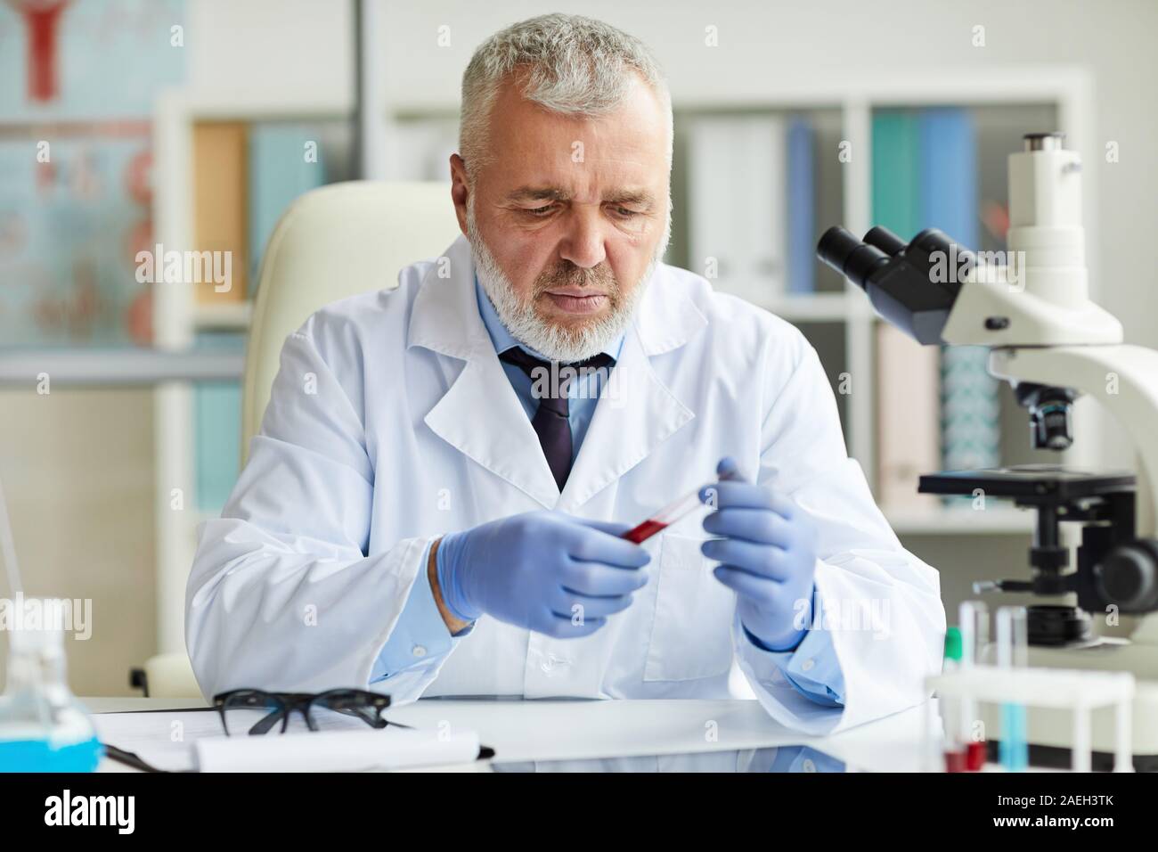 Coppia medico di guanti protettivi di concentrare sul suo lavoro, si è seduta al tavolo e di esaminare i campioni di sangue Foto Stock
