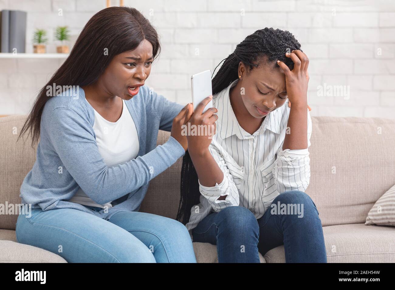 Sconvolto ragazza afro mostra Smartphone con cattivo messaggio alla sua amica Foto Stock